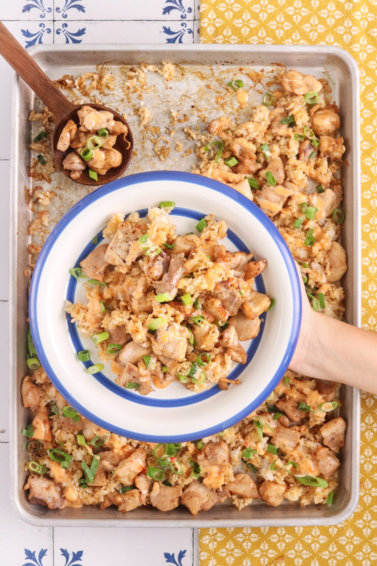 Sheet pan bang bang chicken and crispy rice topped with creamy bang bang sauce and sliced green onions, served on a blue-rimmed plate.