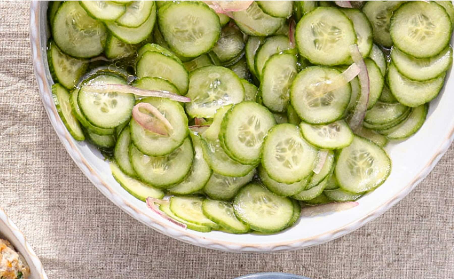 Sliced cucumbers and shallots tossed in a red wine vinaigrette in a white bowl.
