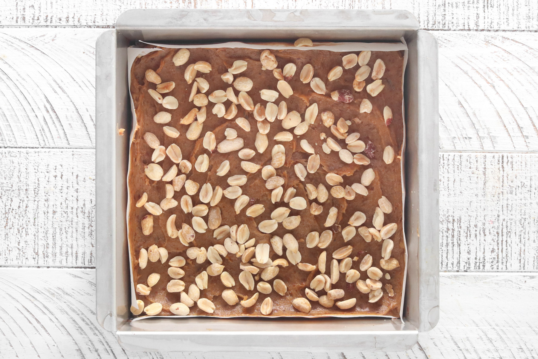 Date caramel layer topped with roasted peanuts in a parchment-lined square pan.