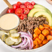 burger bowl with ground beef, roasted sweet potatoes, avocado, cherry tomatoes, pickles, red onion, and creamy burger sauce