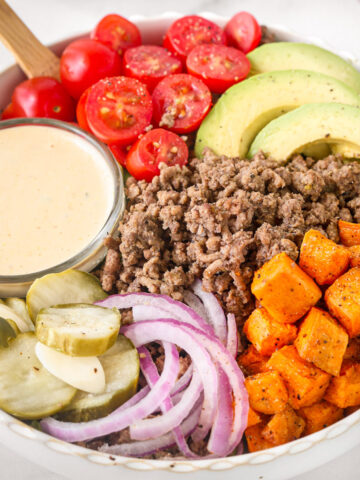 burger bowl with ground beef, roasted sweet potatoes, avocado, cherry tomatoes, pickles, red onion, and creamy burger sauce