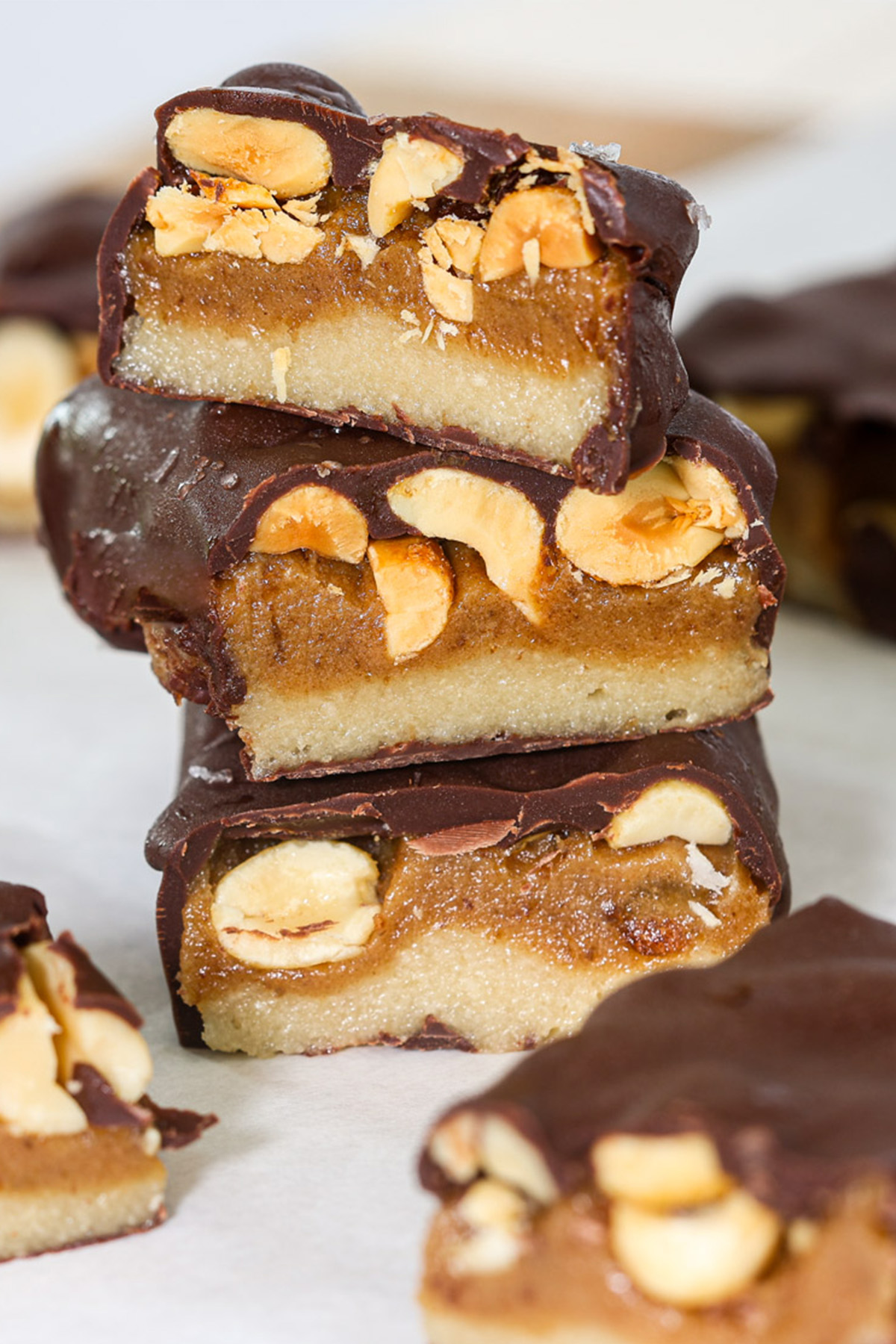 
Stack of three healthy snickers bars cut to show layers of almond flour base, date caramel, and roasted peanuts under a dark chocolate coating.