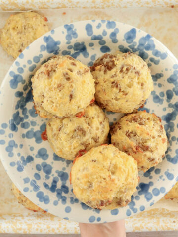 Sausage, egg and cheddar breakfast biscuits arranged on a blue-speckled plate over a yellow baking tray.