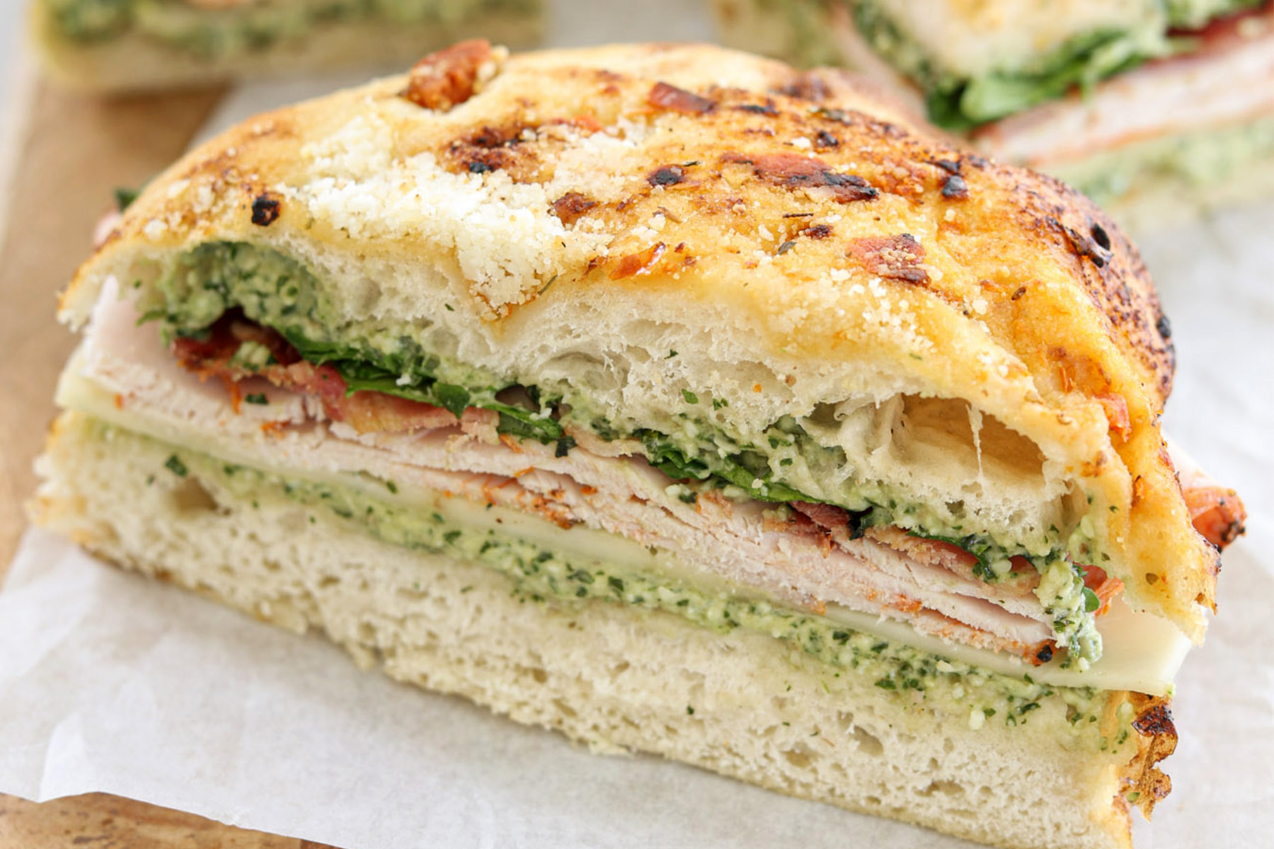 Pressed turkey bacon pesto focaccia sandwich with provolone, arugula, and pesto mayo, sliced and ready to serve.