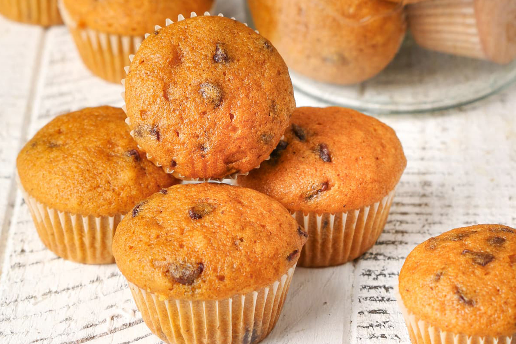 Pumpkin chocolate chip muffins stacked on a white surface with more muffins in the background.