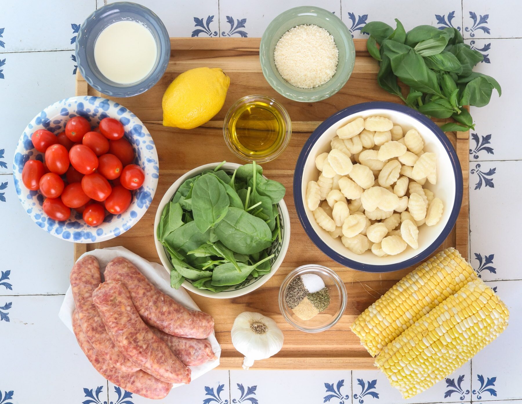 Ingredients for sheet pan gnocchi with sausage, corn and burst tomatoes, including gnocchi, Italian sausage, tomatoes, corn, spinach, basil, Parmesan, cream, lemon and seasonings.