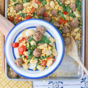 Sheet pan gnocchi with sausage, corn, burst tomatoes and spinach served on a white plate with a blue rim.