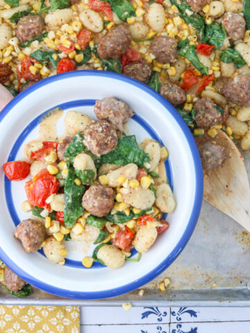 Sheet pan gnocchi with sausage, corn, burst tomatoes and spinach served on a white plate with a blue rim.