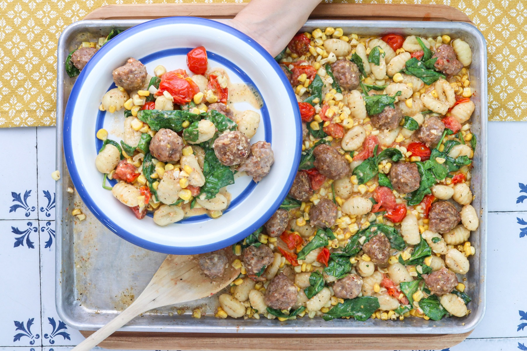 step 4 - Sheet pan gnocchi with sausage, corn, burst tomatoes and spinach being served onto a blue-rimmed plate.