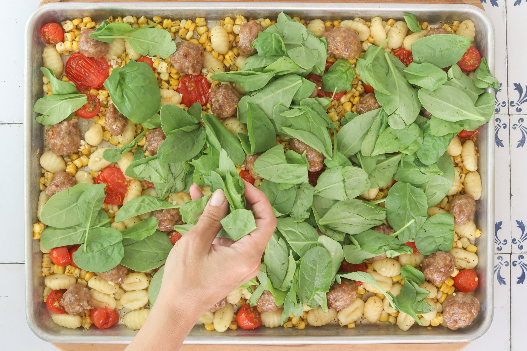 Spinach being added to sheet pan gnocchi with sausage, corn and roasted tomatoes.