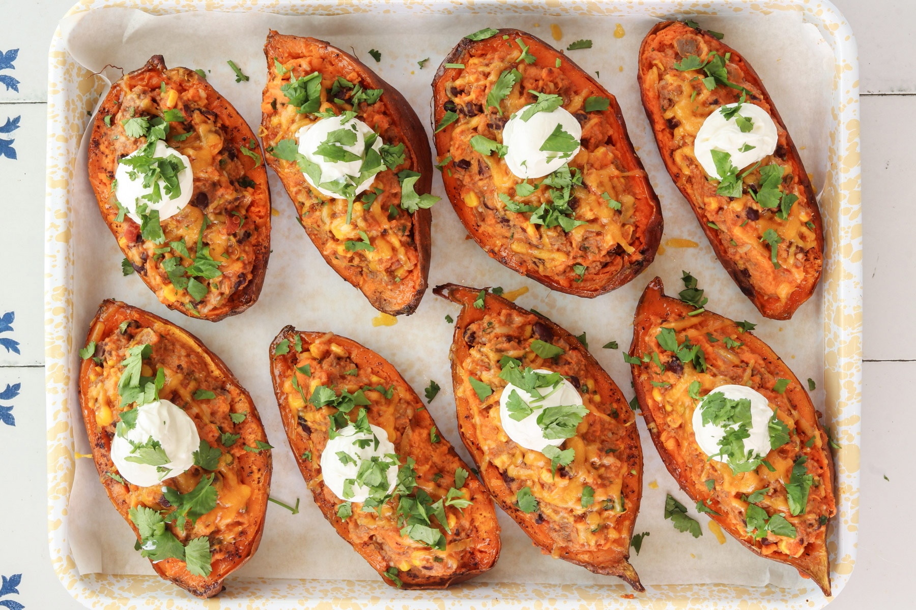 Loaded Mexican sweet potatoes stuffed with ground beef, black beans, corn, and cheese, topped with sour cream and cilantro.