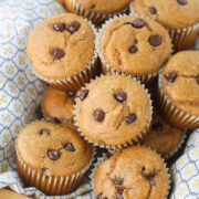 Pumpkin protein muffins with chocolate chips arranged in a yellow baking dish lined with a patterned kitchen towel.