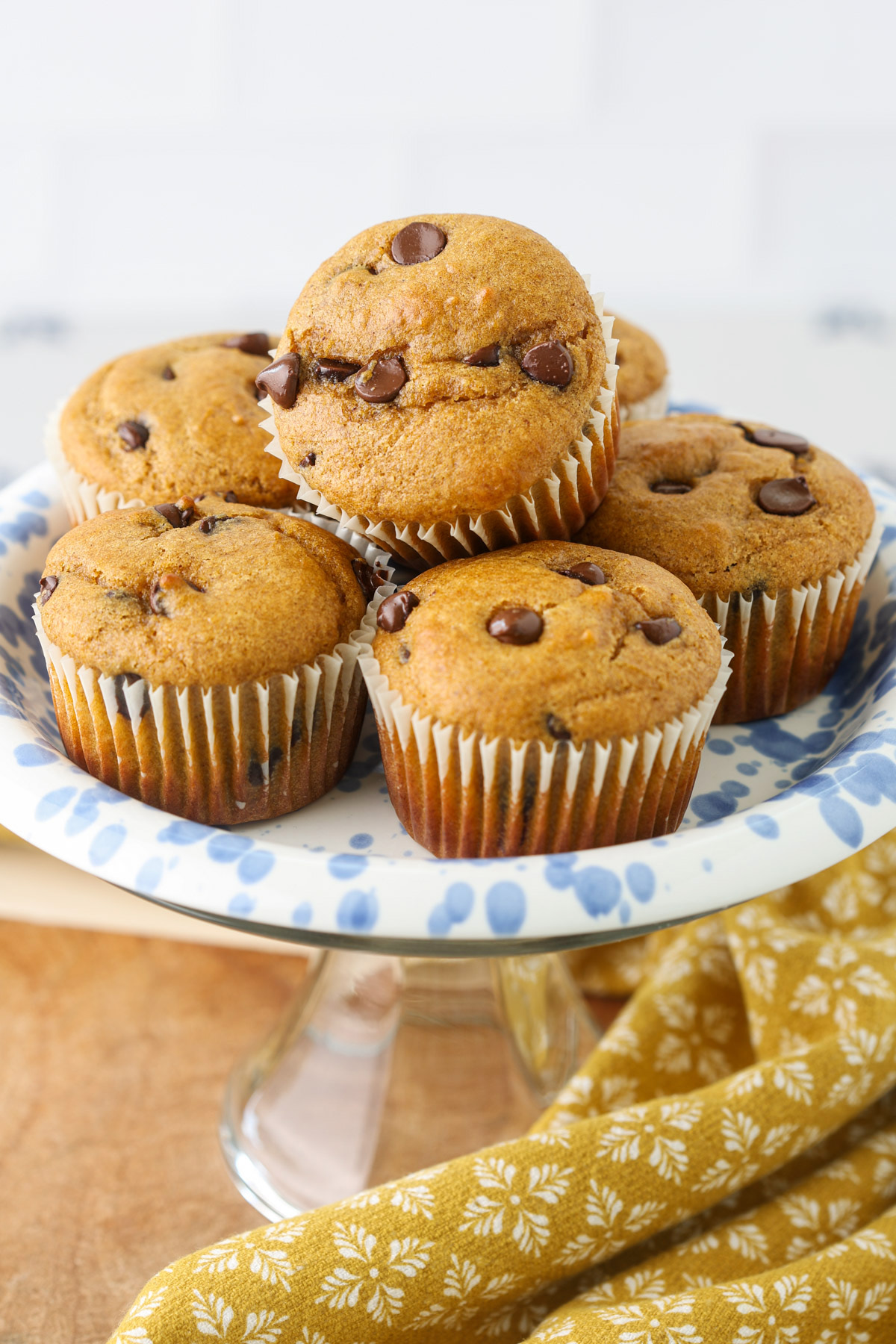 Pumpkin protein muffins with chocolate chips arranged on a blue-and-white cake stand.
