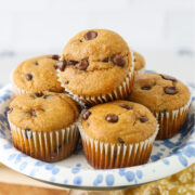 Pumpkin protein muffins with chocolate chips stacked on a blue-and-white plate.