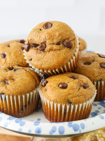 Pumpkin protein muffins with chocolate chips stacked on a blue-and-white plate.