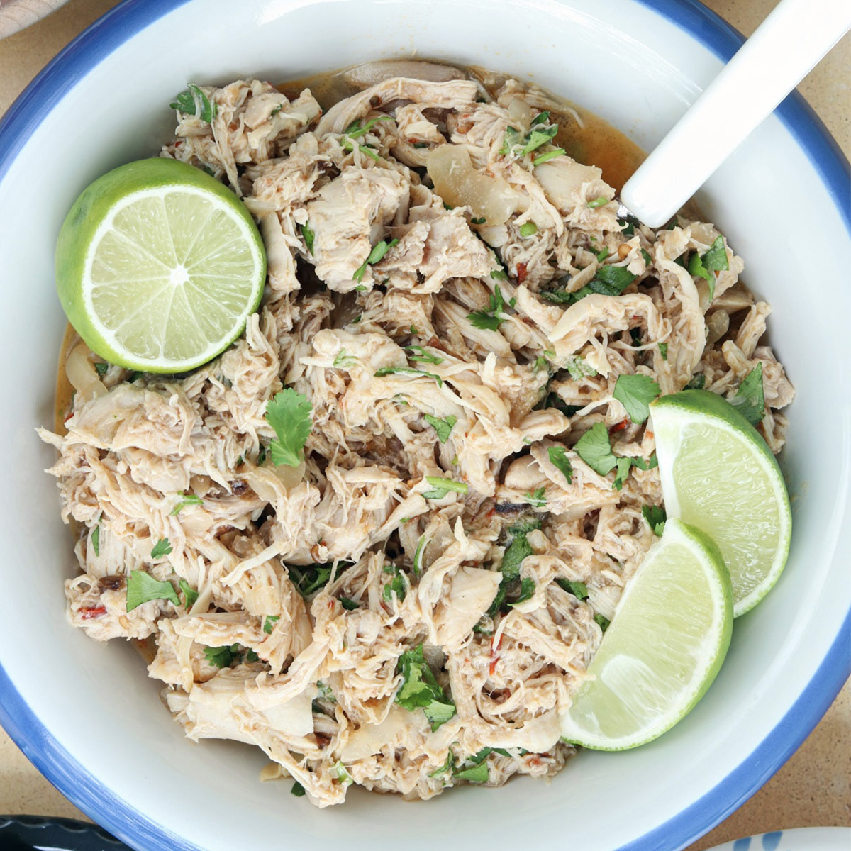 Close-up of slow cooker Mexican shredded chicken topped with cilantro and fresh lime wedges.