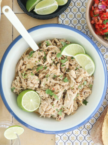 Slow cooker Mexican shredded chicken with lime and cilantro, served with tortillas, rice, tortilla chips, pico de gallo, and lime wedges.