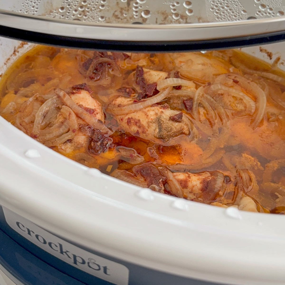 Slow cooker Mexican shredded chicken cooking with onions, chipotle and adobo sauce.