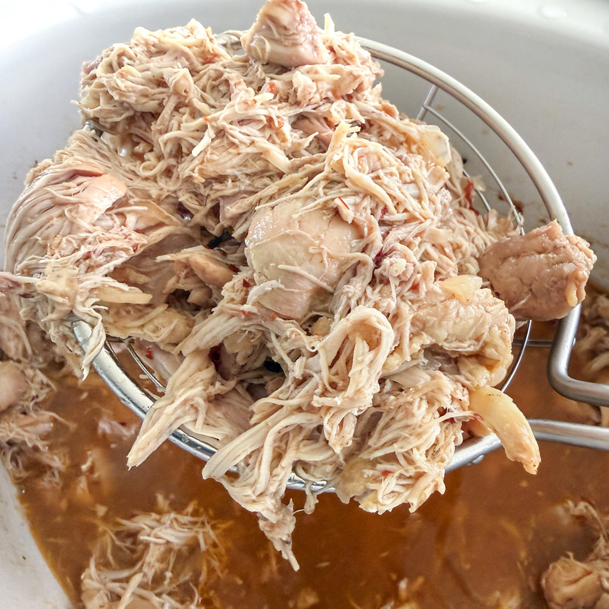 Cooked chicken being lifted from the slow cooker after shredding in the cooking liquid.
