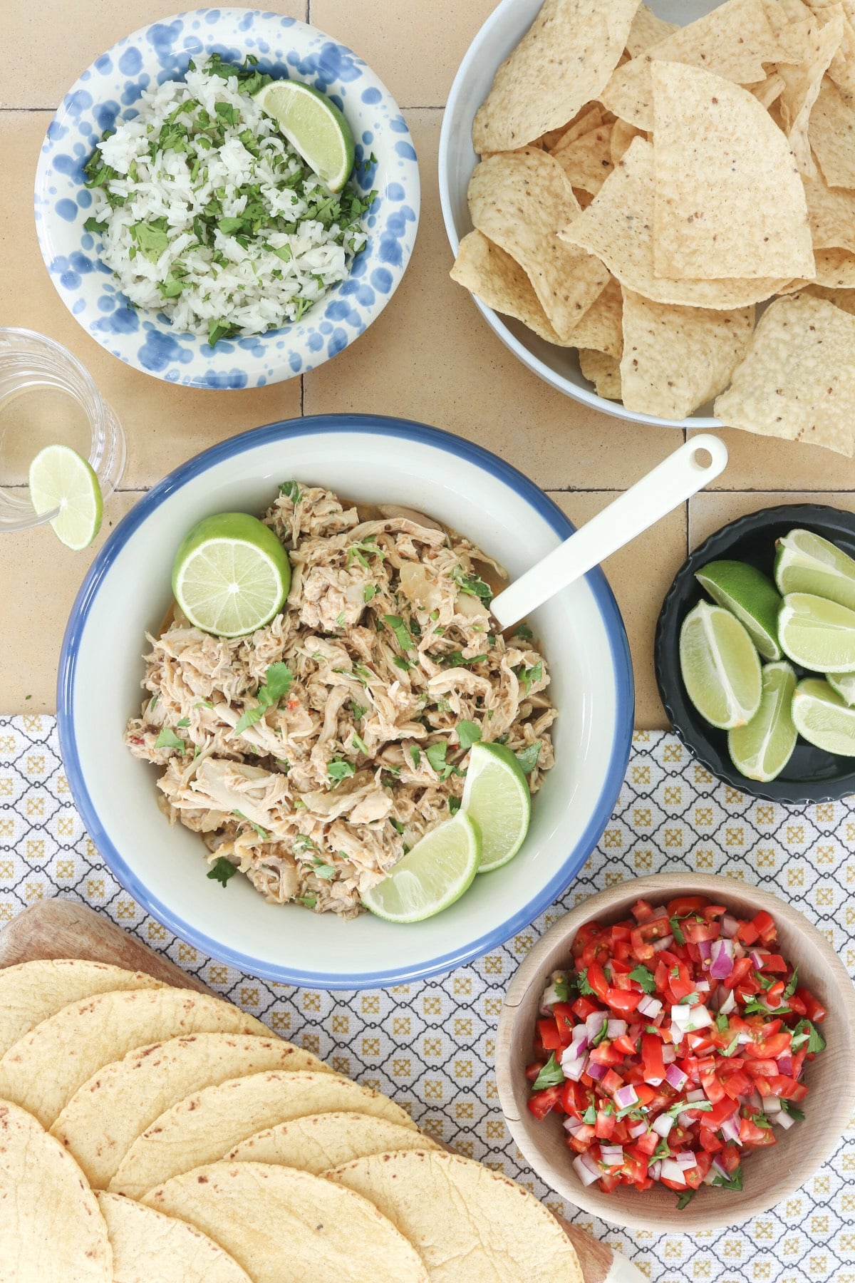 Slow cooker Mexican shredded chicken with lime and cilantro, served with tortillas, rice, tortilla chips, pico de gallo, and lime wedges.