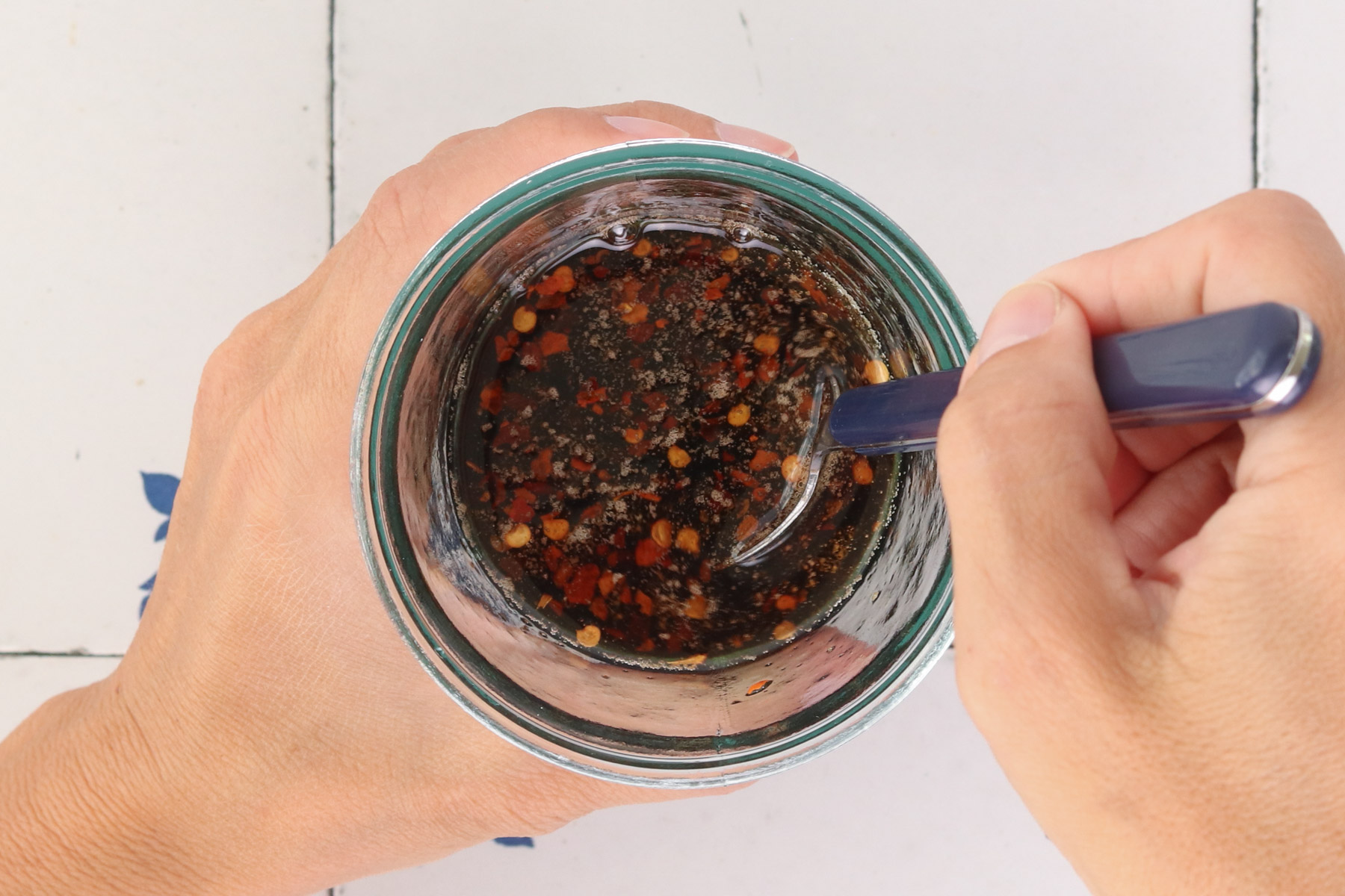 Hands stirring a Korean-style sauce with red pepper flakes in a glass jar for quick Korean beef bowls.