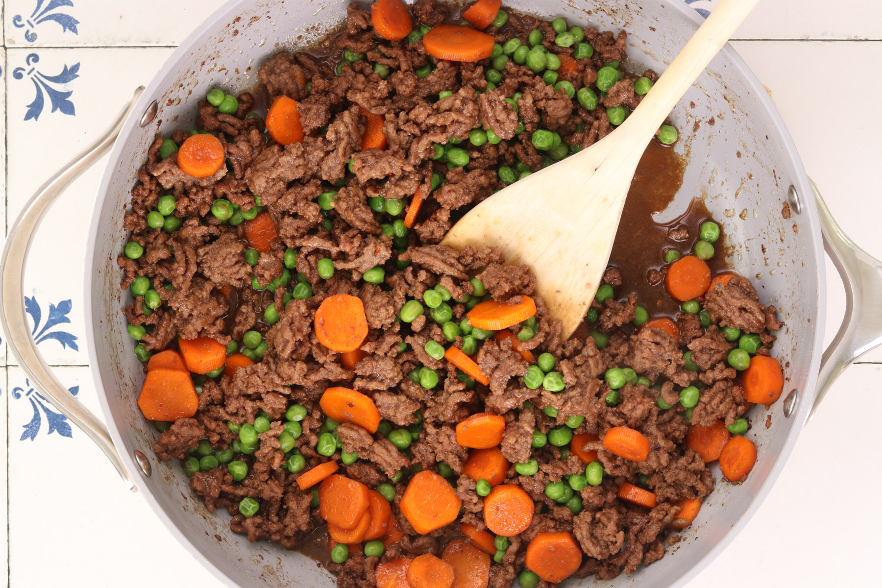 Ground beef with carrots and peas simmering in Korean-style sauce in a skillet.